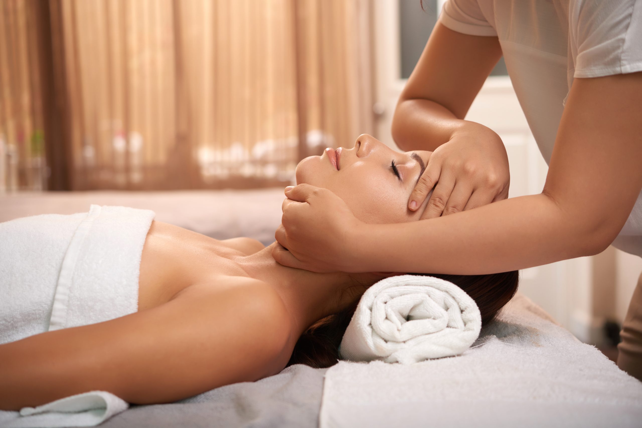 Young woman having calming massage on her face while relaxing in luxurious spa salon